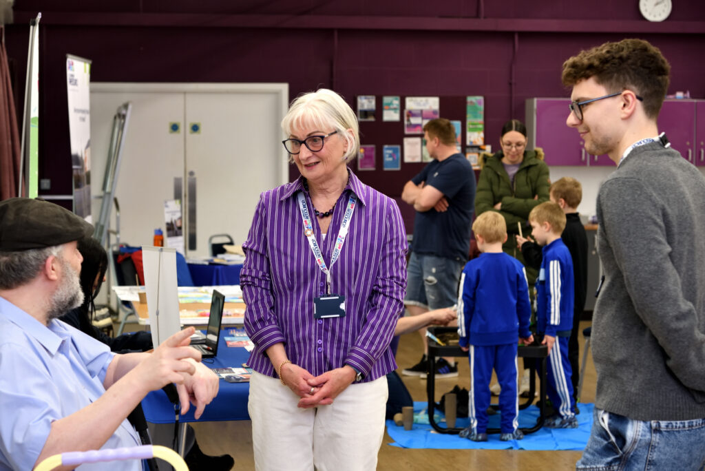 serving-families-fun-day-team-talking-to-an-attendee-in-a-busy-community-hall