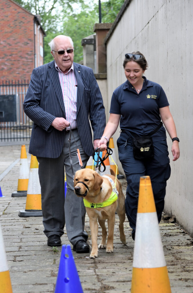 An attendee at the see, hear, remember exhibition working with a guide dog and a member of the Guide Dogs team.